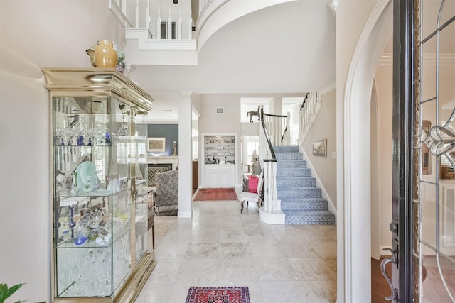 entrance foyer featuring arched walkways, visible vents, stairway, a high ceiling, and ornamental molding