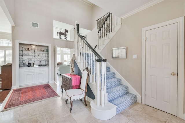 tiled foyer entrance with stairs, ornamental molding, plenty of natural light, and visible vents