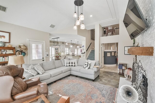 living area featuring a large fireplace, visible vents, stairway, and high vaulted ceiling