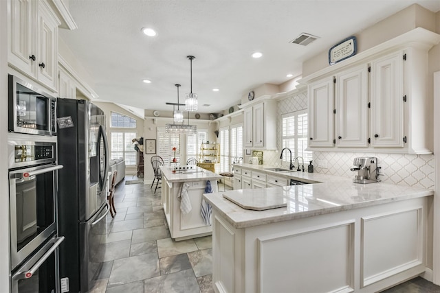 kitchen featuring a peninsula, a sink, visible vents, appliances with stainless steel finishes, and backsplash