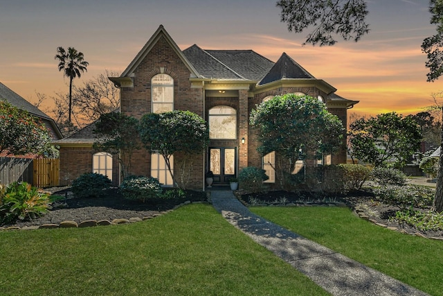 view of front of home featuring brick siding, fence, a lawn, and french doors