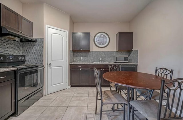 kitchen featuring dark brown cabinetry, black appliances, under cabinet range hood, and light stone countertops