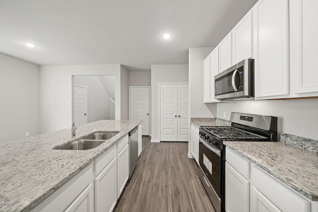 kitchen with white cabinets, light stone countertops, stainless steel appliances, and a sink