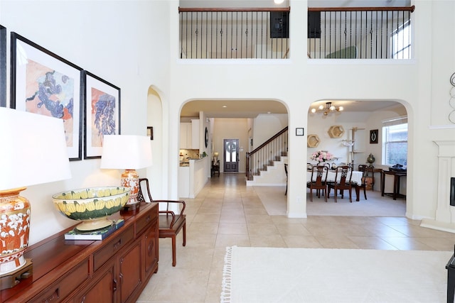 entryway featuring arched walkways, light tile patterned floors, stairway, and a towering ceiling