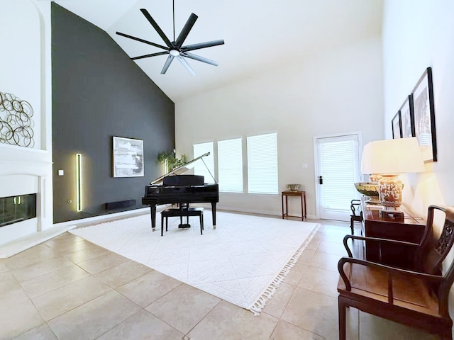 living area with baseboards, a glass covered fireplace, ceiling fan, tile patterned floors, and high vaulted ceiling