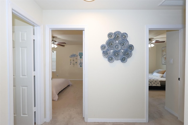 hall with baseboards, visible vents, and light colored carpet