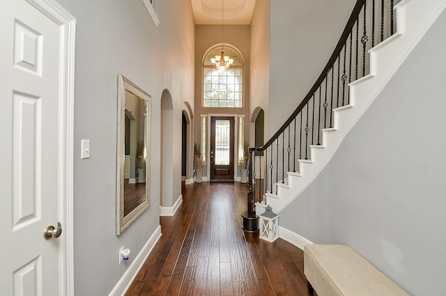 foyer featuring a chandelier, a towering ceiling, baseboards, stairs, and dark wood-style floors