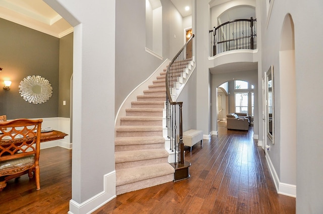 entrance foyer with arched walkways, wood-type flooring, a high ceiling, baseboards, and stairs