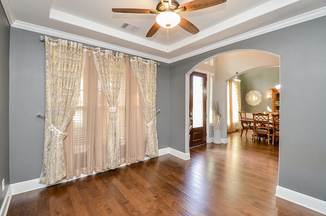 unfurnished room featuring wood-type flooring, visible vents, a raised ceiling, and arched walkways