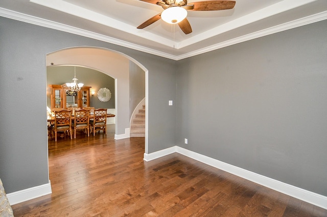 empty room featuring a tray ceiling, arched walkways, hardwood / wood-style floors, ornamental molding, and baseboards