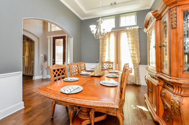 dining space with arched walkways, a raised ceiling, dark wood-style flooring, and a chandelier