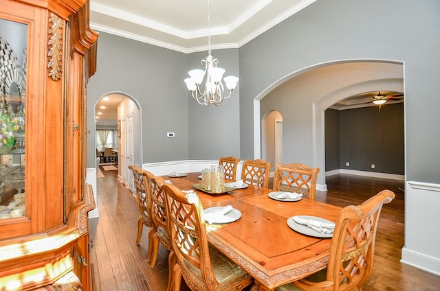 dining area featuring dark wood-type flooring, arched walkways, a tray ceiling, and ceiling fan with notable chandelier