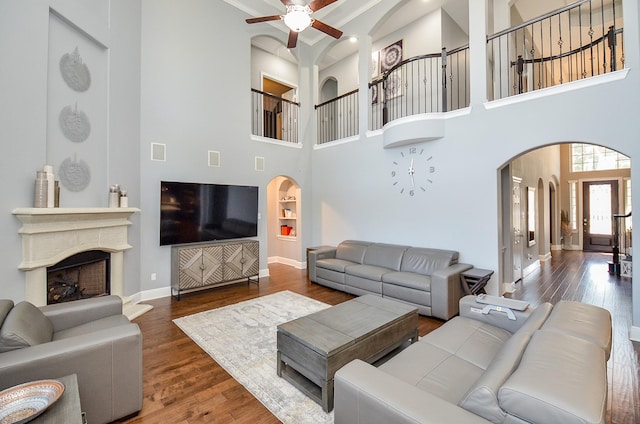 living room featuring arched walkways, a fireplace with raised hearth, baseboards, and wood finished floors