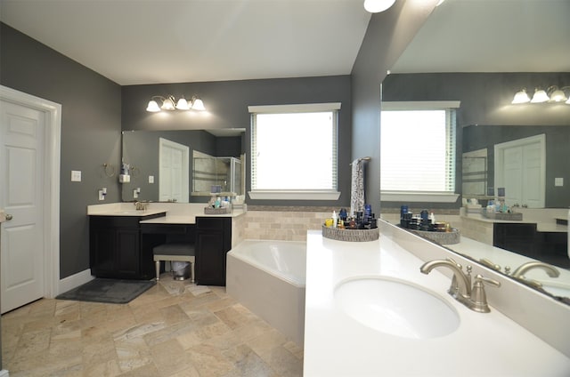 bathroom with a stall shower, two vanities, a sink, stone finish flooring, and a bath