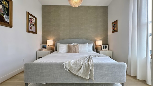 bedroom featuring an accent wall, light wood finished floors, and baseboards