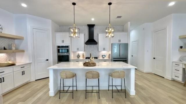 kitchen with wall chimney exhaust hood, stainless steel appliances, light countertops, white cabinetry, and open shelves