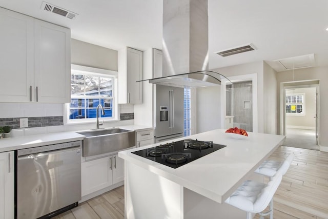 kitchen with island range hood, a sink, visible vents, white cabinetry, and appliances with stainless steel finishes