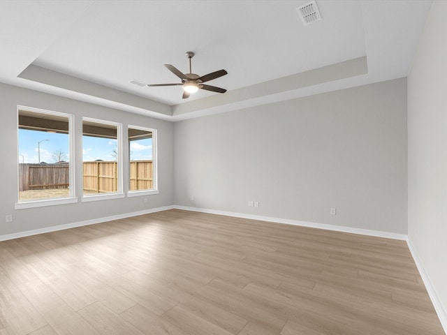 spare room with light wood finished floors, a raised ceiling, visible vents, and baseboards