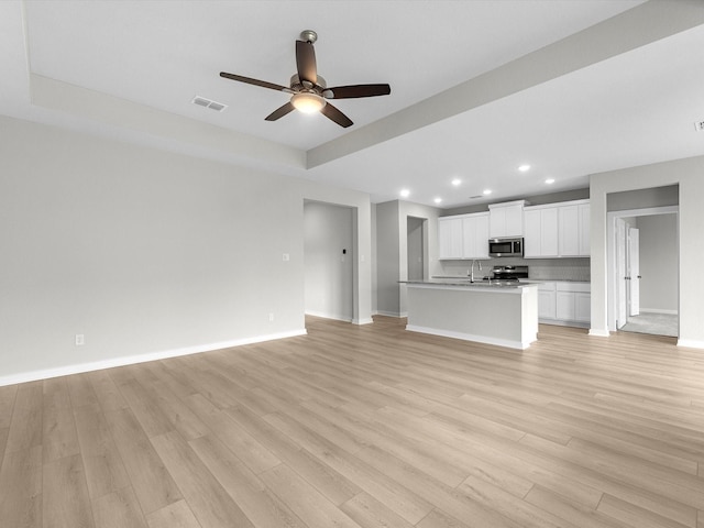 unfurnished living room with a sink, light wood-style flooring, a raised ceiling, and visible vents