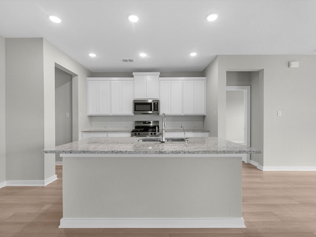 kitchen with a sink, white cabinets, appliances with stainless steel finishes, light stone countertops, and a center island with sink