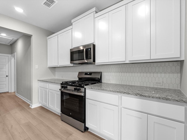 kitchen with visible vents, white cabinets, light stone countertops, stainless steel appliances, and light wood-style floors