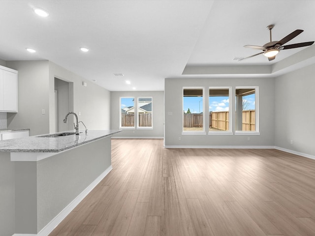 unfurnished living room with light wood finished floors, baseboards, a ceiling fan, a sink, and recessed lighting