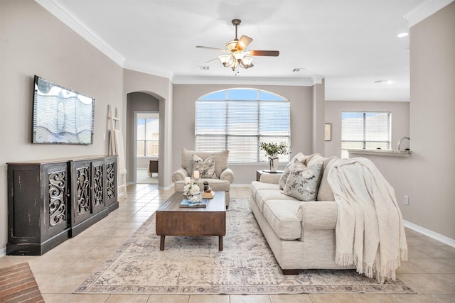 living area with arched walkways, light tile patterned floors, ornamental molding, a ceiling fan, and baseboards