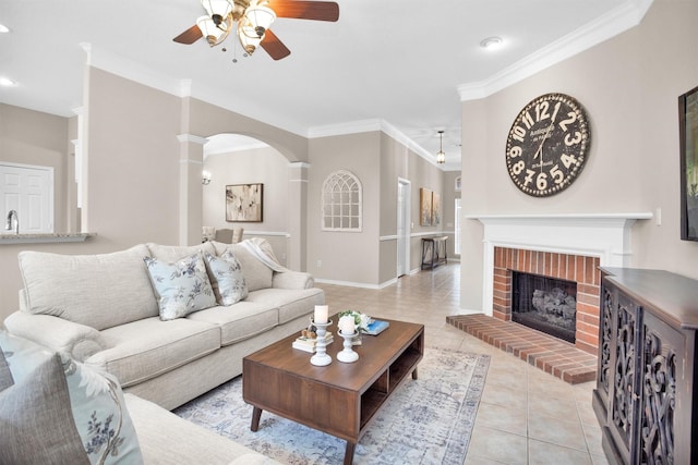 living area featuring light tile patterned floors, arched walkways, a ceiling fan, ornamental molding, and a fireplace