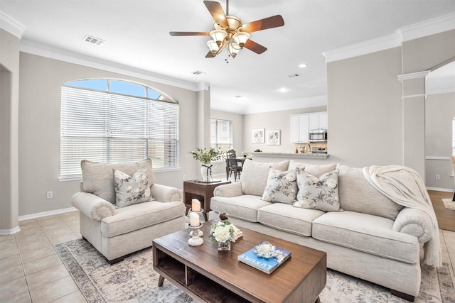 living area featuring light tile patterned floors, visible vents, baseboards, ceiling fan, and crown molding