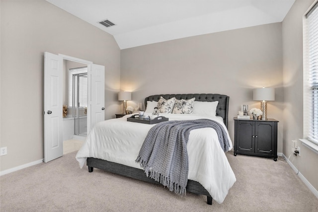 bedroom featuring lofted ceiling, light colored carpet, visible vents, ensuite bath, and baseboards