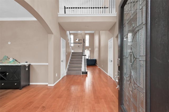 foyer featuring arched walkways, stairway, a high ceiling, light wood-style floors, and baseboards