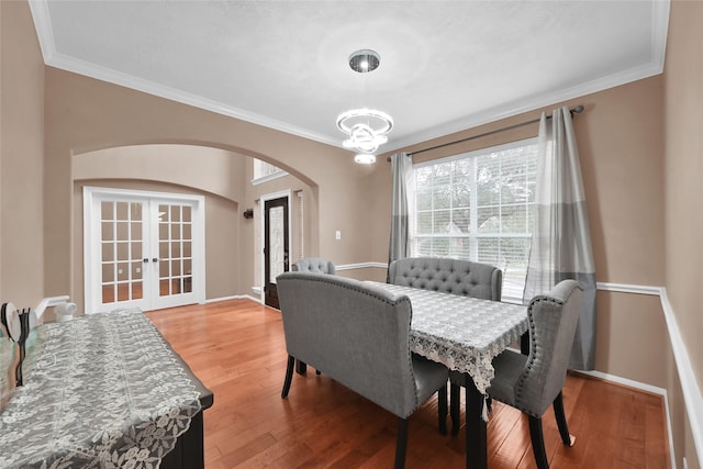 dining space with arched walkways, french doors, a notable chandelier, ornamental molding, and wood finished floors