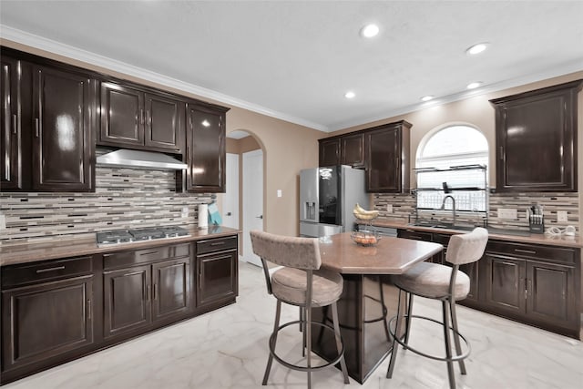 kitchen with arched walkways, marble finish floor, appliances with stainless steel finishes, dark brown cabinets, and under cabinet range hood