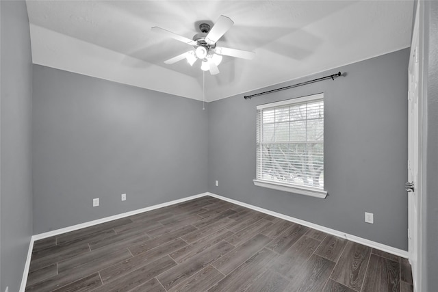 spare room featuring dark wood-style flooring, a ceiling fan, and baseboards
