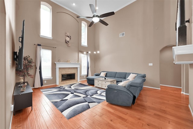 living room featuring baseboards, arched walkways, a ceiling fan, a glass covered fireplace, and light wood-type flooring