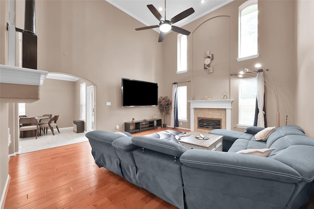 living room with arched walkways, ceiling fan, a fireplace, wood finished floors, and crown molding