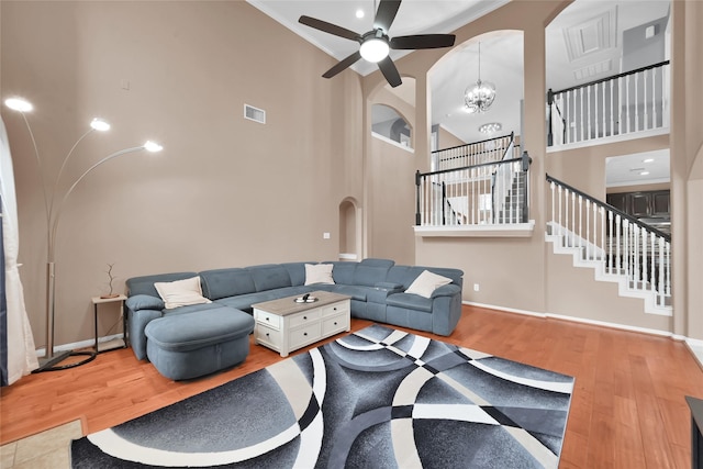 living room with arched walkways, a high ceiling, visible vents, light wood-style floors, and stairway