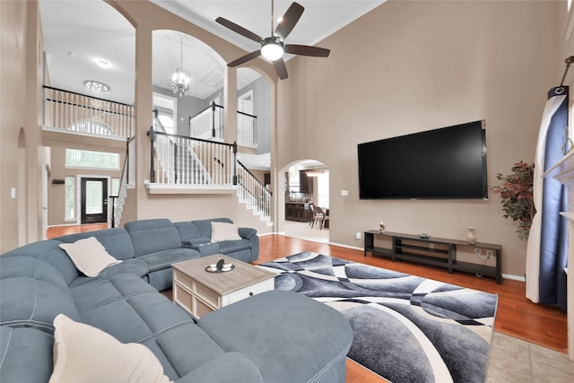 living room featuring arched walkways, wood finished floors, stairway, ceiling fan with notable chandelier, and a high ceiling