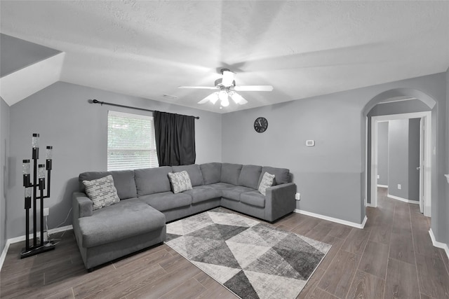 living room featuring baseboards, arched walkways, a ceiling fan, dark wood-style floors, and a textured ceiling