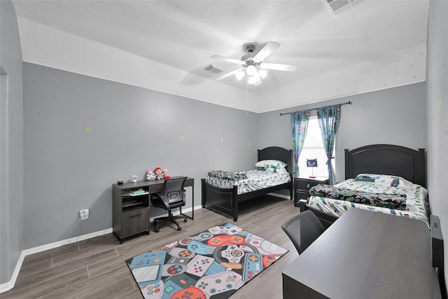 bedroom with ceiling fan, wood finished floors, visible vents, and baseboards