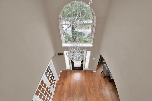 foyer with hardwood / wood-style floors, a chandelier, a healthy amount of sunlight, and a towering ceiling