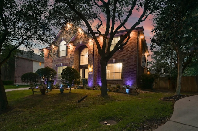 traditional home featuring a lawn, fence, stone siding, and brick siding