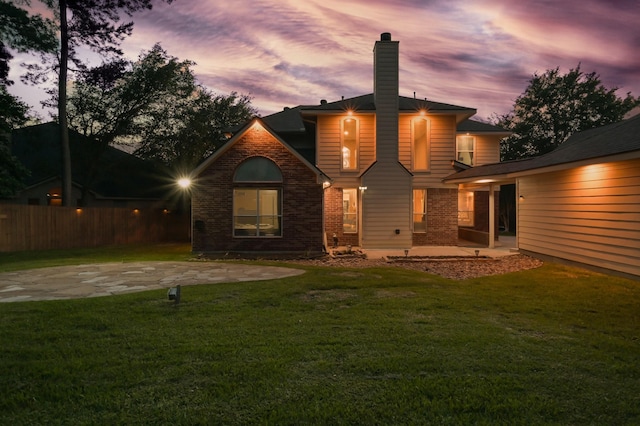 rear view of house featuring fence, a patio, a chimney, brick siding, and a yard