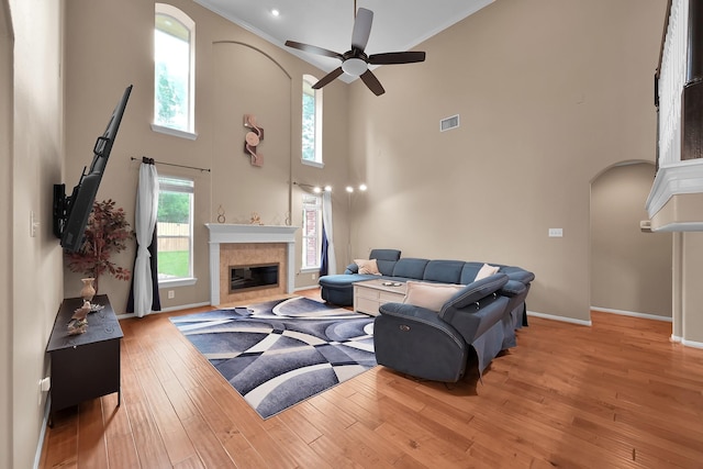 living area featuring ceiling fan, visible vents, a towering ceiling, arched walkways, and a tile fireplace