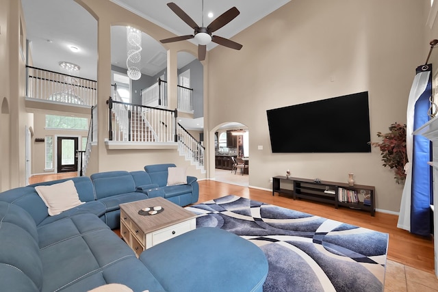 living room featuring a high ceiling, arched walkways, stairs, a ceiling fan, and wood finished floors