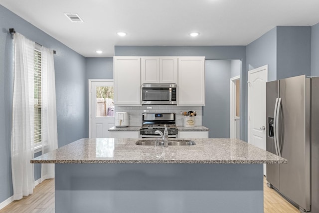 kitchen with appliances with stainless steel finishes, white cabinets, an island with sink, and light stone countertops