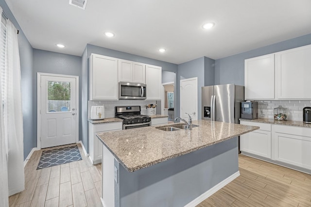 kitchen featuring appliances with stainless steel finishes, a sink, a center island with sink, and white cabinets