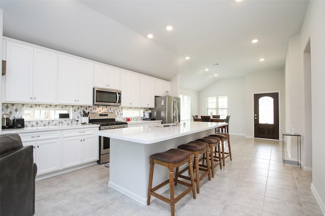 kitchen featuring stainless steel appliances, white cabinets, light countertops, and a center island with sink