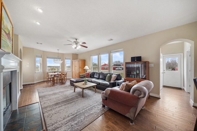 living area with arched walkways, dark wood-type flooring, visible vents, baseboards, and a glass covered fireplace