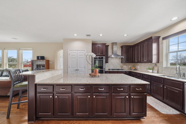 kitchen with wall chimney exhaust hood, a kitchen breakfast bar, dark wood-type flooring, dark brown cabinets, and a sink